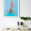 Cinthya art print by Zanate displayed in a white frame above a modern desk – vibrant pink Venus figure on sky-blue background